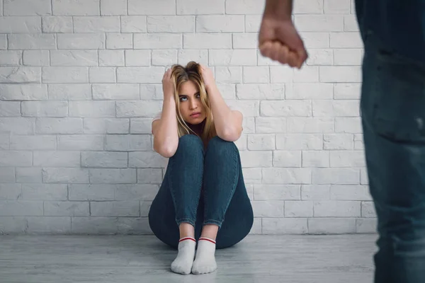 Alto a la violencia doméstica. Mujer sentada en el suelo, cubre la cabeza con las manos y mira al marido con el puño cerrado — Foto de Stock