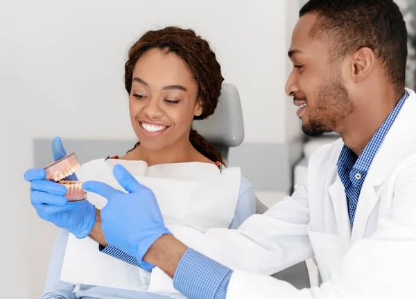 Siyah yakışıklı dişçi kadın hasta plastik çene gösteriyor. — Stok fotoğraf