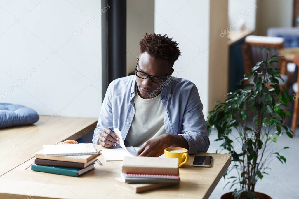 Hardworking African American student working on research in university canteen