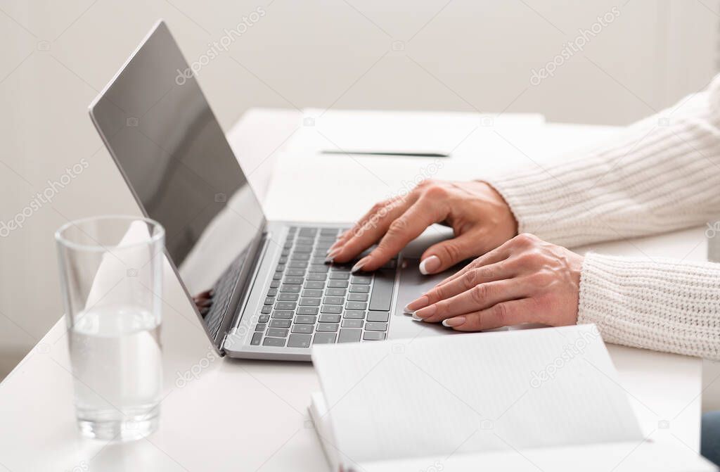 Work online and operating on computer. On table are laptop, notebooks, glass of water