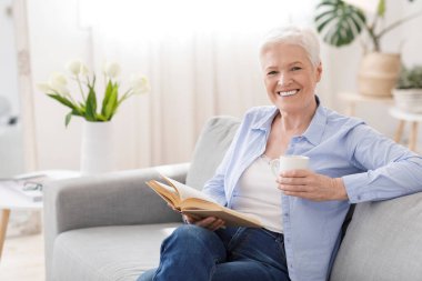 Favori eğlencesi. Yaşlı kadın evde kitap ve sıcak çayla dinleniyor.