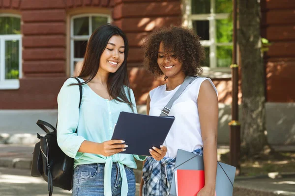 两名多文化女学生站在大学校园附近，手里拿着工作手册 — 图库照片