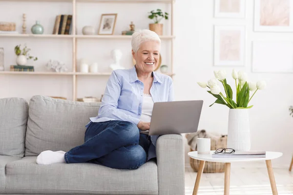 Lächelnde ältere Dame entspannt sich mit Laptop auf Couch zu Hause — Stockfoto