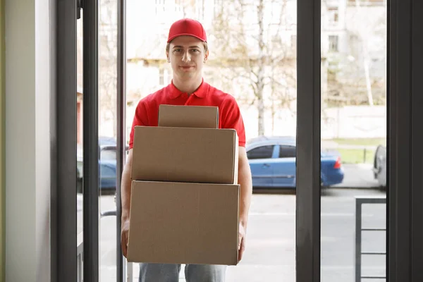 Pedido en línea y servicio postal moderno. Mensajero en uniforme rojo sostiene muchas cajas — Foto de Stock