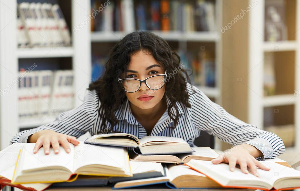 Tired student leaning on books in the campus library
