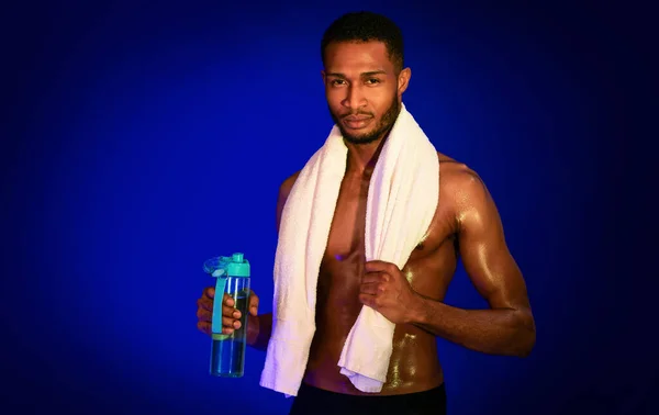 Atleta africano cara segurando garrafa de água posando, fundo azul — Fotografia de Stock