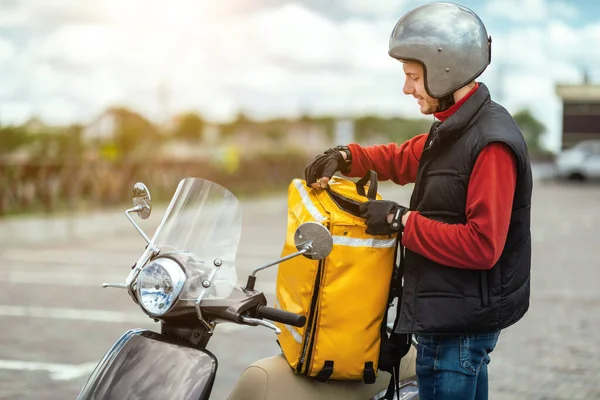 Entrega cara abertura saco de pé perto de moto entrega refeições fora — Fotografia de Stock