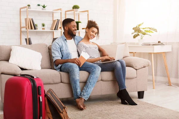 Černý pár pomocí notebooku sedí s cestovním kufříkem doma — Stock fotografie