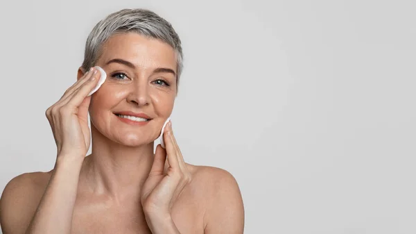 Cuidados com a pele maduro. Mulher de meia-idade bonita removendo maquiagem com almofadas de algodão — Fotografia de Stock