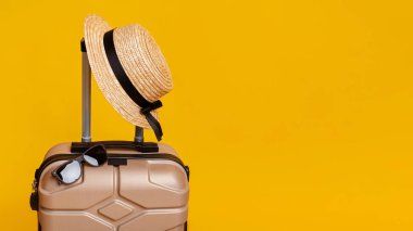 Yaz Gezisi. Güneş gözlüklü bavul ve sarı arka planda şapka.