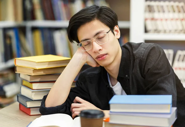 Prüfungszeit. Erschöpfter japanischer Student in Brille schläft in der Bibliothek zwischen Stapeln voller Bücher, Kopierraum — Stockbild Müdes Studentenschläfchen in der Universitätsbibliothek — Stockfoto