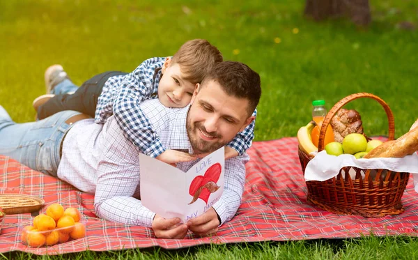 Celebrando el Día del Padre. Joven padre emocionado de leer la tarjeta de felicitación de sus hijos durante el picnic en el campo — Foto de Stock