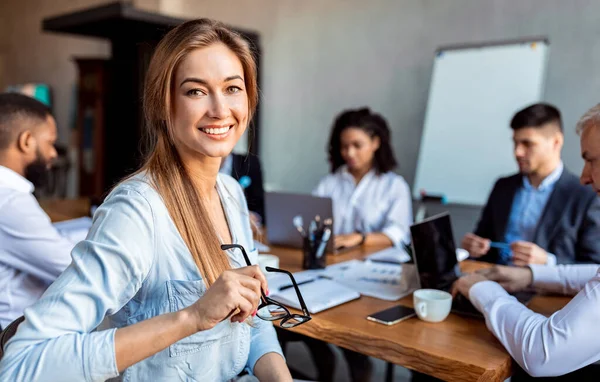 Empresária sorrindo sentada em reunião com colegas de trabalho no escritório — Fotografia de Stock