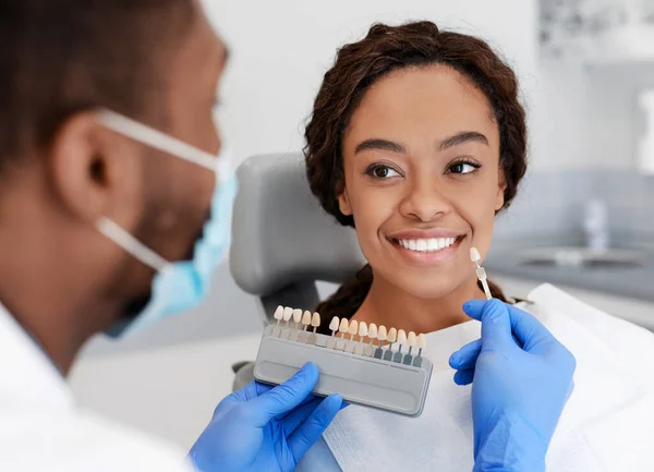 Siyahi doktor, gülümseyen genç bayanın üzerinde diş ölçeği örneği tutuyor. — Stok fotoğraf
