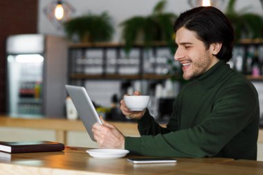 Dijital tablet kullanan ve kahve içen neşeli adam.