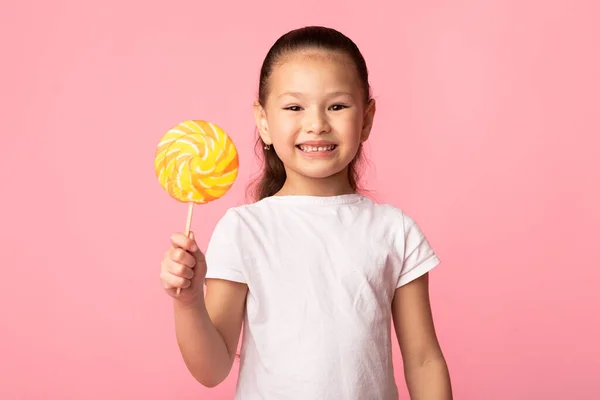 Adorable chica asiática sonriendo y sosteniendo colorida piruleta — Foto de Stock