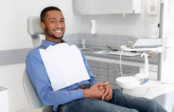 Szczęśliwy czarny facet siedzi na krześle dentystycznym, uczęszcza do kliniki dentystycznej — Zdjęcie stockowe