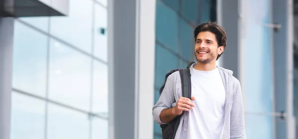 Joven sonriente con mochila al aire libre cerca del edificio del aeropuerto — Foto de Stock
