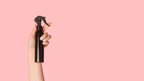 Vista ritagliata della mano ragazza che mostra bottiglia spray nero con prodotto cosmetico su sfondo rosa, spazio copia — Foto Stock