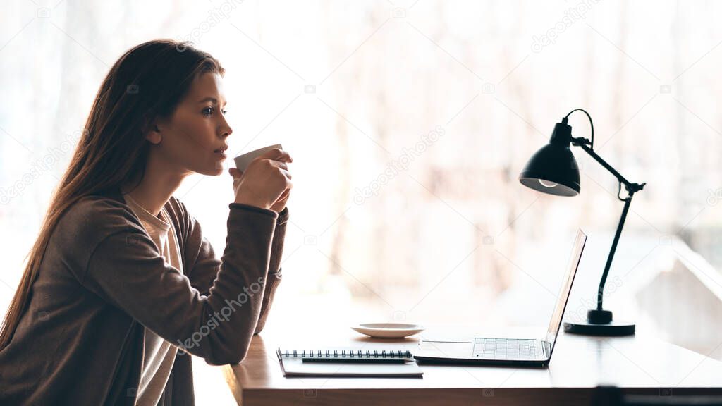 Young woman holding coffee mug, using laptop