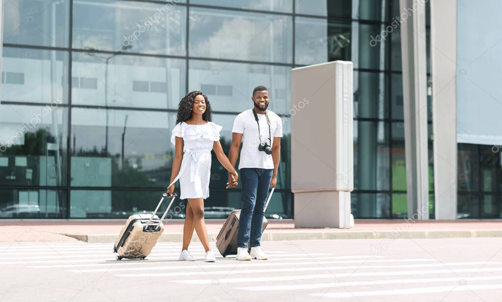 Happy african american newlyweds walking out of airport building with luggage