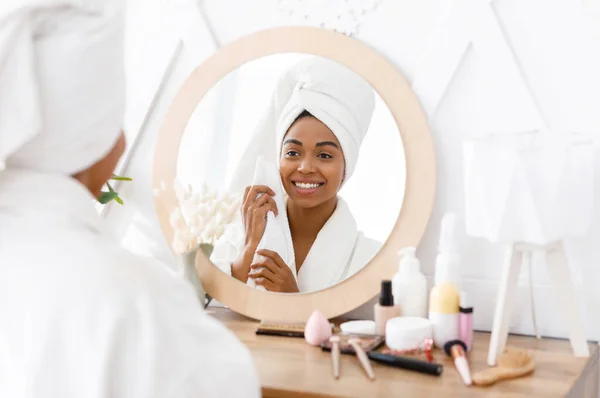 Beautiful black woman with towel on head drying face, looking in mirror — Stock Photo, Image