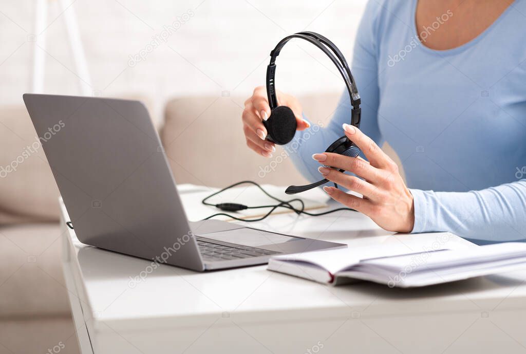 Beginning of working day of online consultant. Woman holds headphones in her hands, near laptop and notebook on table