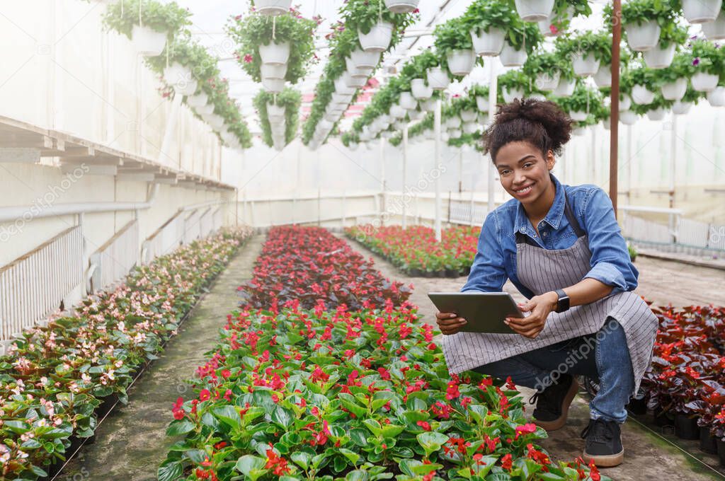 Modern technologies for farmers and growing flowers. Girl with tablet in hands sits near flowers