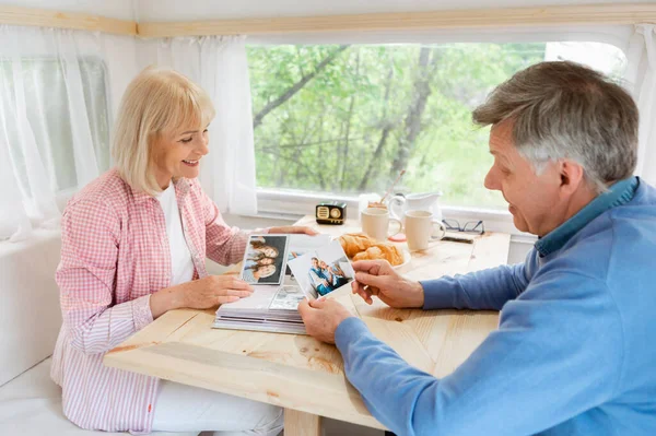 Senioren-Ehepaar blättert im Familienalbum mit Fotos im Inneren des Wohnmobils — Stockfoto