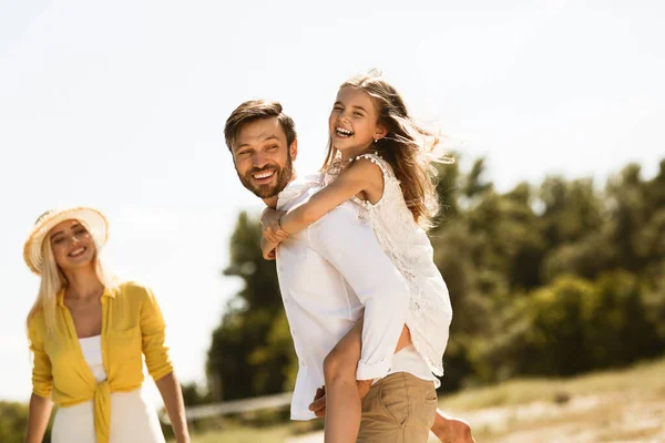 Família feliz desfrutando do dia de verão juntos, pai carregando filha ao ar livre — Fotografia de Stock