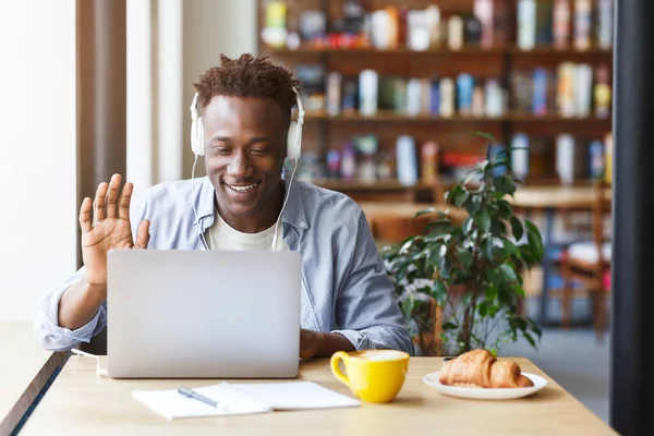 Allegro uomo afroamericano con cuffie che comunicano in videochat al caffè urbano, copia lo spazio — Foto Stock