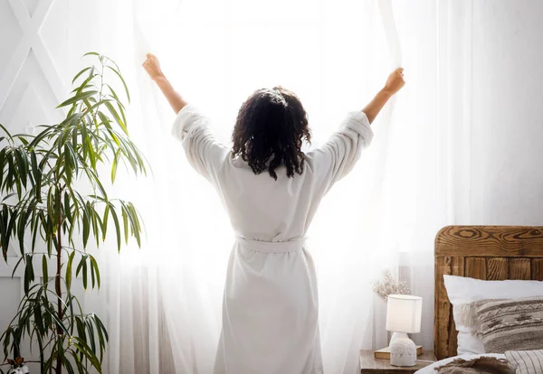 Mañana perfecta. Mujer irreconocible en bata blanca abriendo cortinas de ventana en casa —  Fotos de Stock