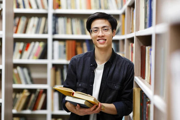 Mosolygó koreai fickó könyvekkel a könyvtárban. — Stock Fotó