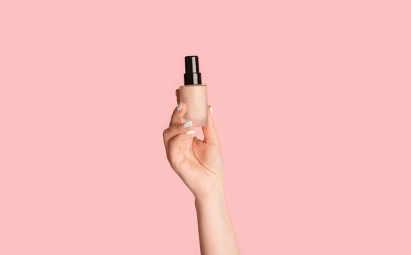 Beskuren bild av tusenårig flicka visar flaska makeup foundation på rosa bakgrund — Stockfoto