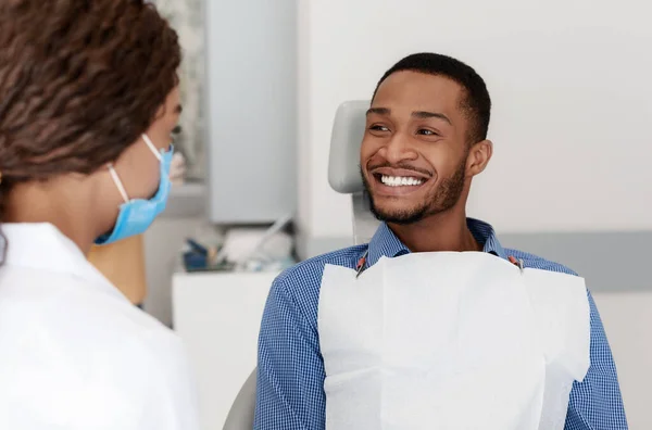 Joven hombre negro sonriendo a médico dentista femenino — Foto de Stock