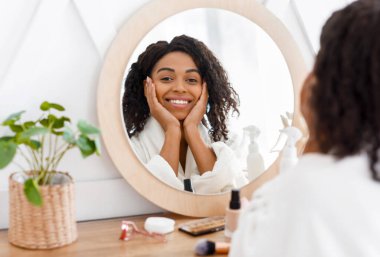 Beautiful Black Woman In Bathrobe Sitting At Dresser Table, Looking To Mirror clipart