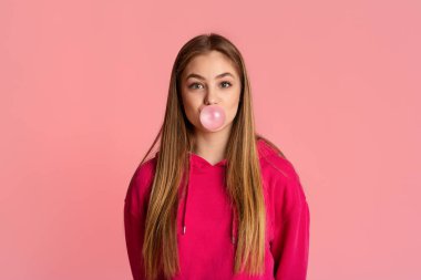 Pembe kapüşonlu tatlı kız, sakız baloncuğu çıkarıyor.