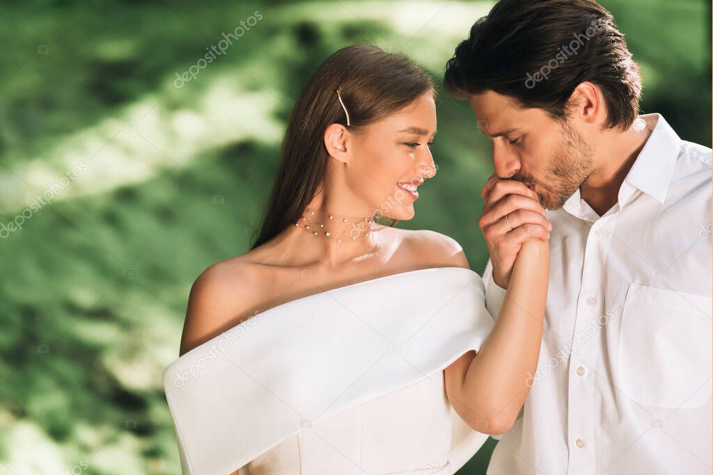 Loving Groom Kissing Brides Hand Standing In Beautiful Park