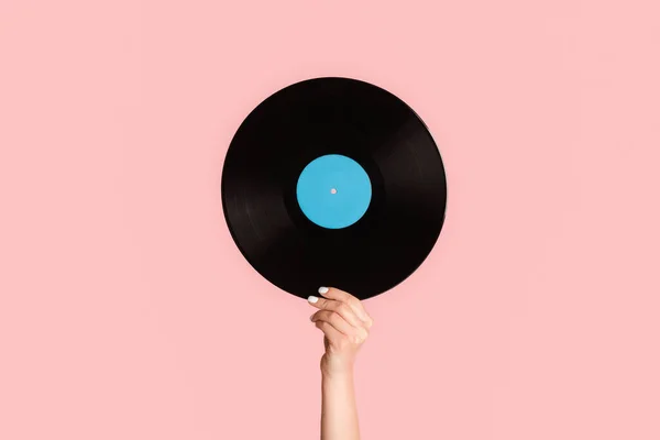 Girl hand showing retro vinyl gramophone record on pink background, closeup