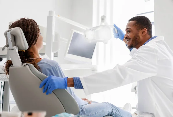 Dentista masculino alegre falando com mulher sentada na cadeira do dentista — Fotografia de Stock