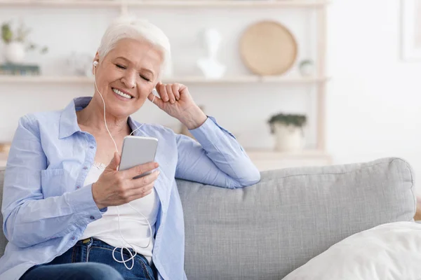 Aposentadoria despreocupada. Mulher sênior ouvir música no smartphone com fones de ouvido em casa — Fotografia de Stock