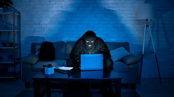 Hacker mascarado baixar informações privadas usando laptop — Fotografia de Stock