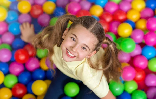 Счастливая девочка с пончиками, играющая в шариковой яме на детской площадке, вид сверху — стоковое фото
