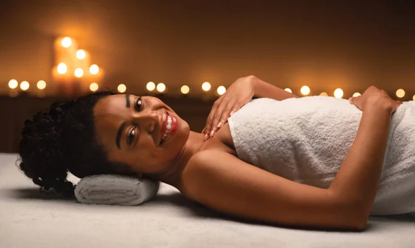 Foto panorâmica de mulher negra sorridente que coloca na mesa de massagem — Fotografia de Stock