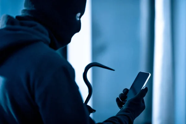 Vilão segurando pé de cabra e smartphone preparando roubo — Fotografia de Stock