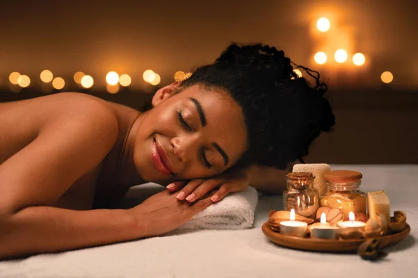 Smiling african woman lying on massage table at spa — Stock Photo, Image