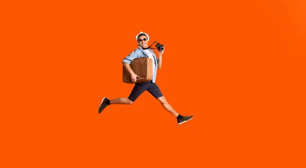 Happy photographer with suitcase running fast over orange background