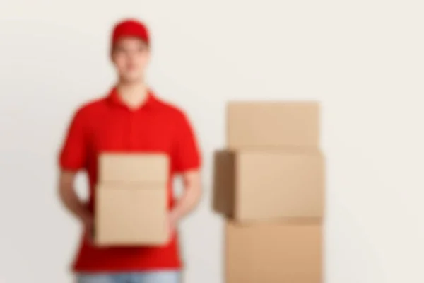 Foto borrosa de mensajero en uniforme rojo, sostiene paquetes, cerca de pila de cajas — Foto de Stock