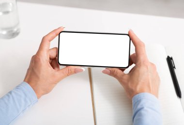 İş için akıllı telefonu kullanmak. Kadın elleri telefonu beyaz masaüstünde tutuyor