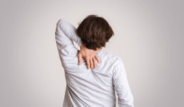 Kaşıntı ve alerji. Sırtını kaşıyan bir adam var. Gri arka planda tek başına.